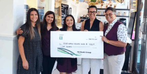 ATIRA leadership meeting with donors in a café setting, holding a large symbolic bank cheque stand, all smiling to represent corporate giving