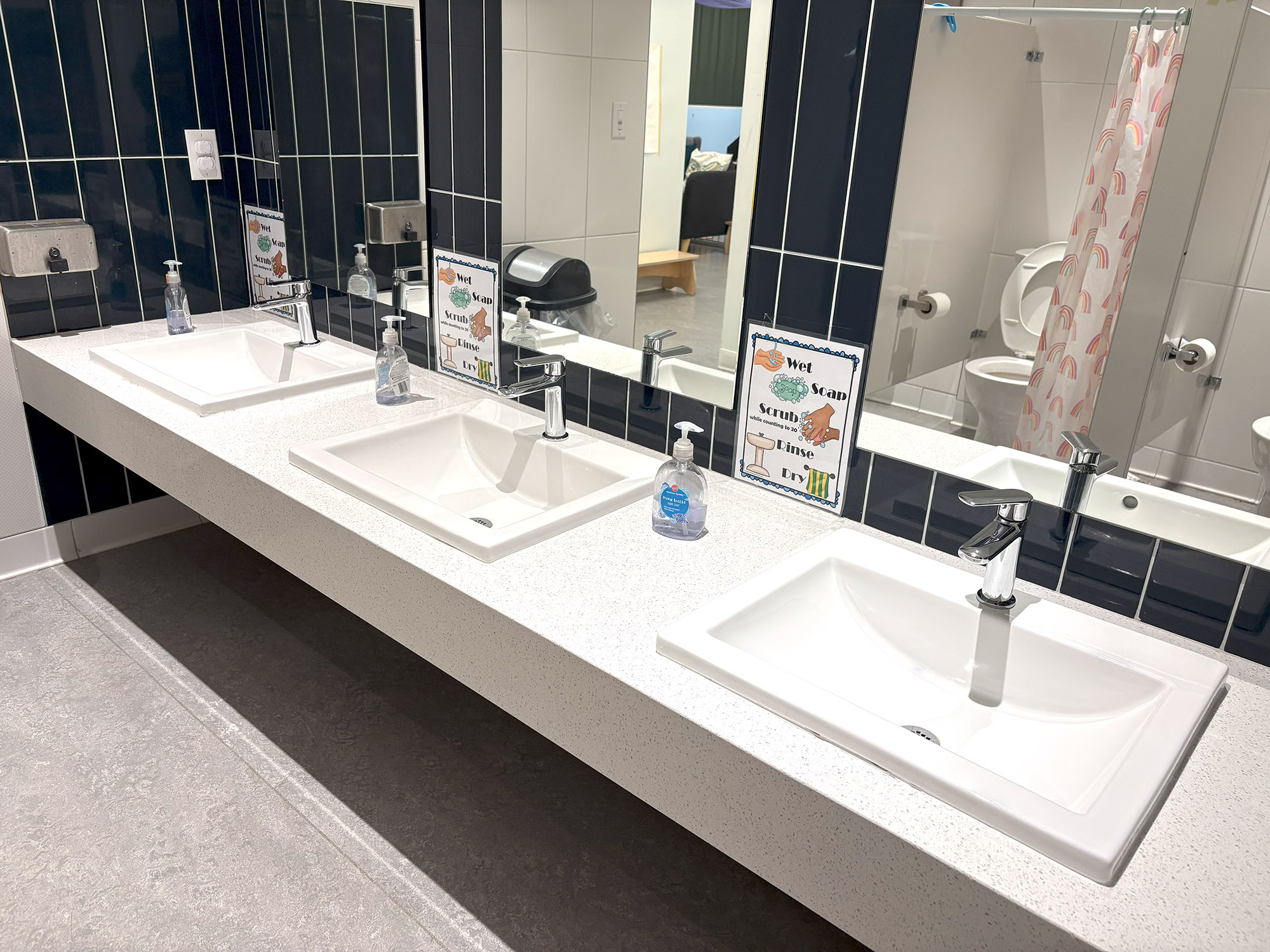 A clean and organized children’s bathroom with instructional posters showing proper handwashing techniques