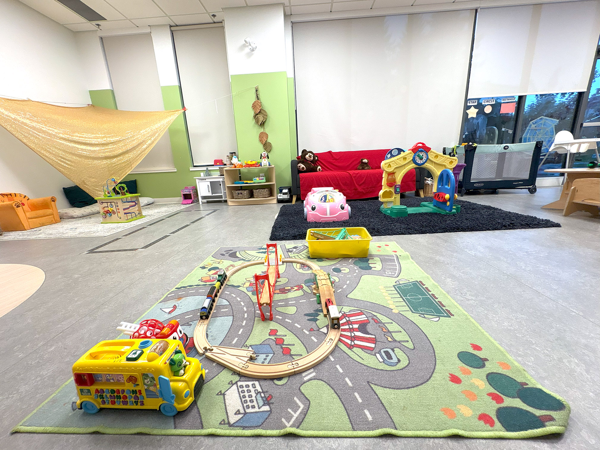 A large children’s playroom with various toys such as dolls and toy cars, a train set, and wooden shelves