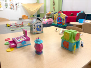 Colorful toys for children aged 3–6 placed on a wooden table in a large playroom equipped with recreational and educational facilities