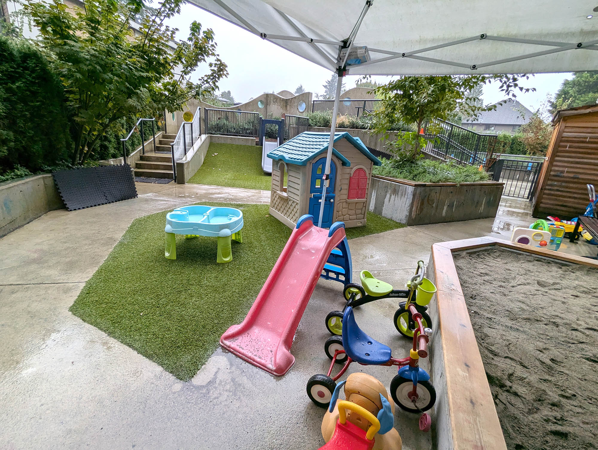 A playground area in front of a building with a slide and several tricycles