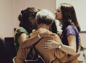 Four women of different ages embracing each other in a supportive gesture, representing empathy, connection, and solidarity.
